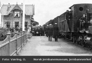 Fra perrongen på Hamar stasjon med ankommende persontog trukket av damplok type VI i spor 1. En gruppe (sangere?) oppstilt for fotografering. 1880-85